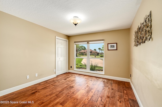unfurnished room featuring baseboards, a textured ceiling, and wood finished floors