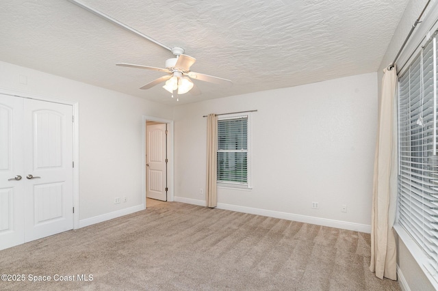 unfurnished bedroom featuring light carpet, baseboards, ceiling fan, a textured ceiling, and a closet
