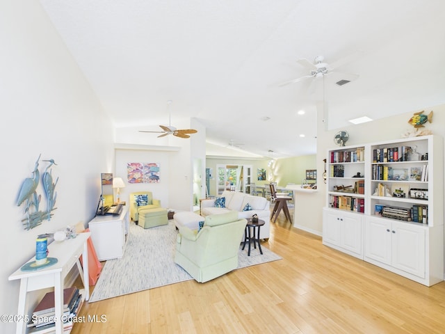 living area featuring vaulted ceiling with skylight, light wood-style flooring, and a ceiling fan