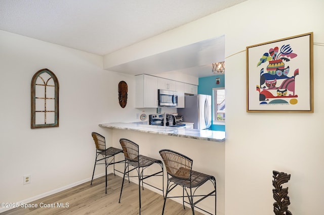 2245 Golf Isle Dr Unit 424, Melbourne, FL 32935 - kitchen with white cabinets, stainless steel appliances, a peninsula, light wood-style floors, and a breakfast bar