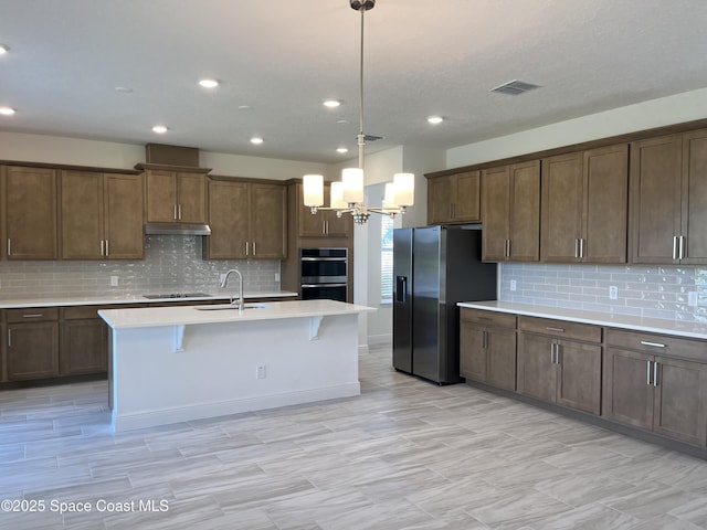 kitchen with visible vents, a sink, light countertops, under cabinet range hood, and stainless steel appliances