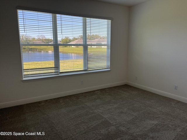 unfurnished room with a water view, baseboards, and dark colored carpet