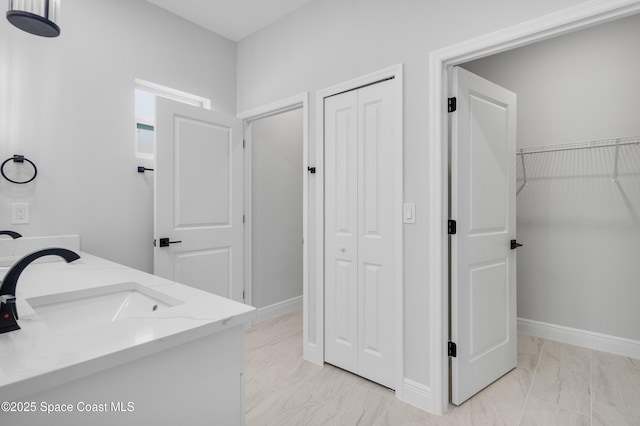 bathroom featuring double vanity, marble finish floor, baseboards, and a sink