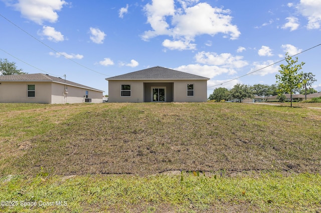 back of house featuring stucco siding and a lawn