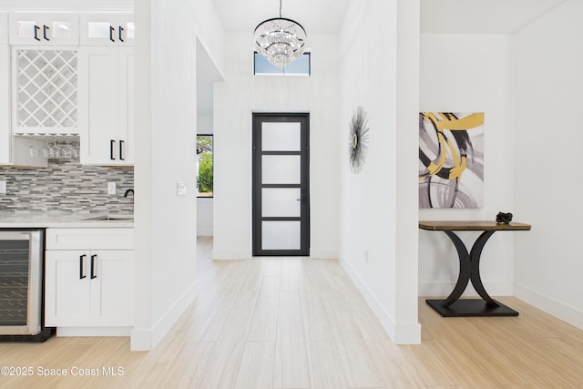 entryway with indoor bar, an inviting chandelier, beverage cooler, and light wood-style floors