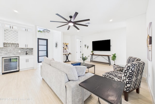 living room featuring light wood-style flooring, wet bar, visible vents, ceiling fan, and beverage cooler