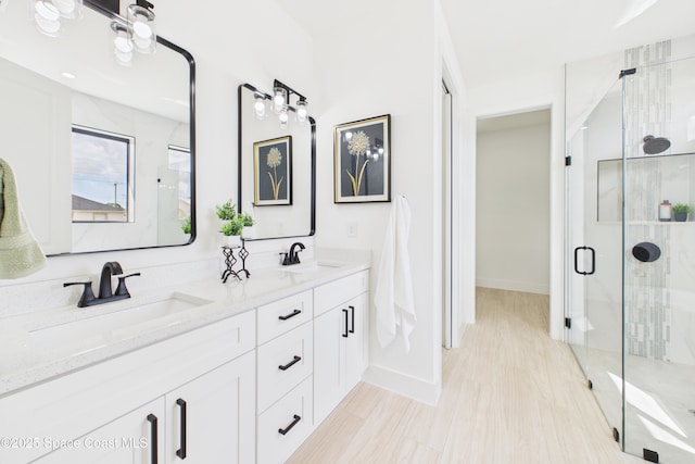 bathroom featuring baseboards, double vanity, a stall shower, and a sink