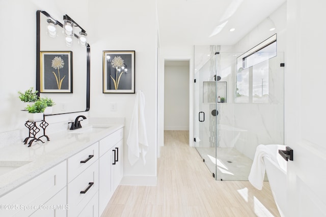 bathroom featuring a freestanding bath, double vanity, a marble finish shower, a sink, and baseboards