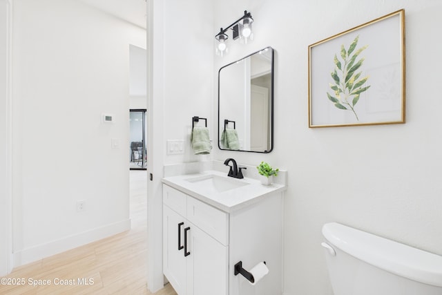 bathroom with baseboards, wood finished floors, vanity, and toilet