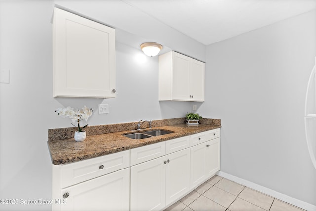 kitchen featuring light tile patterned floors, white cabinetry, dark stone countertops, a sink, and baseboards