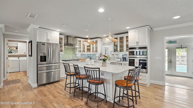 235 Northgrove Dr, Merritt Island, FL 32953 - kitchen featuring stainless steel appliances, washer and clothes dryer, wall chimney exhaust hood, ornamental molding, and a breakfast bar