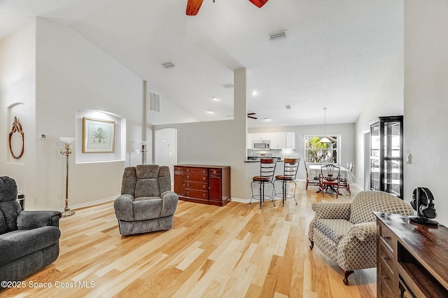 living area with lofted ceiling, visible vents, light wood-type flooring, and ceiling fan