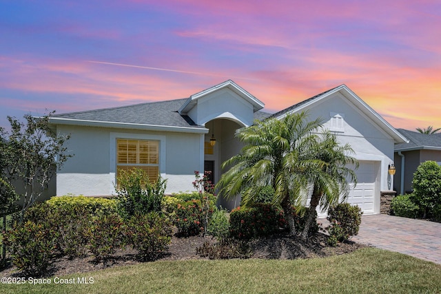 ranch-style house featuring a garage, a shingled roof, stucco siding, and decorative driveway