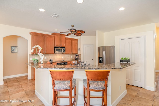 1472 Bent Palm Dr, Merritt Island, FL 32952 - kitchen with appliances with stainless steel finishes, ceiling fan, backsplash, a kitchen bar, and dark stone countertops