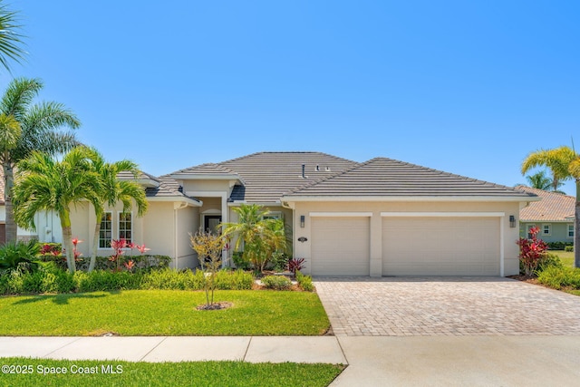 ranch-style house with an attached garage, a tile roof, stucco siding, a front yard, and decorative driveway