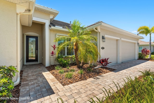 entrance to property with an attached garage, decorative driveway, and stucco siding