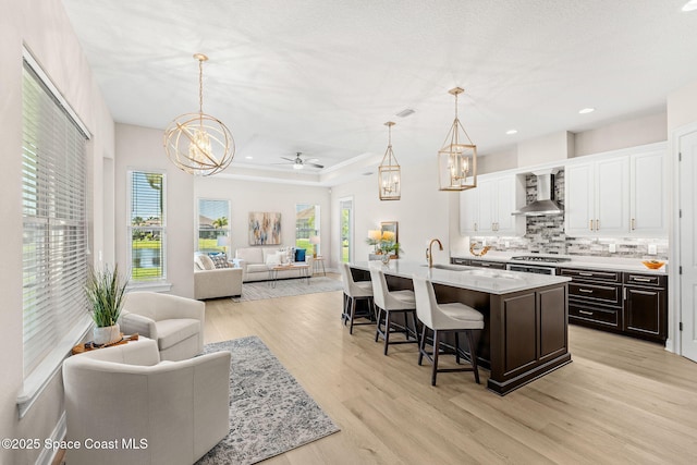 kitchen featuring plenty of natural light, wall chimney exhaust hood, ceiling fan with notable chandelier, open floor plan, and tasteful backsplash