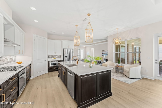kitchen with a sink, appliances with stainless steel finishes, white cabinets, and light wood-style flooring