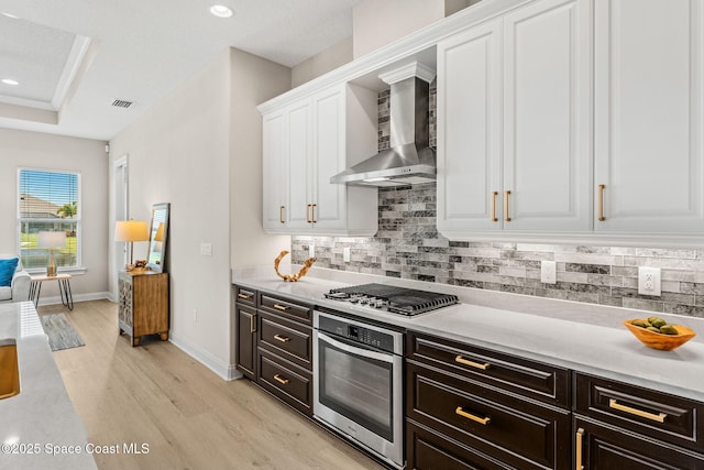 kitchen featuring wall chimney range hood, visible vents, light wood-style floors, stainless steel appliances, and white cabinetry