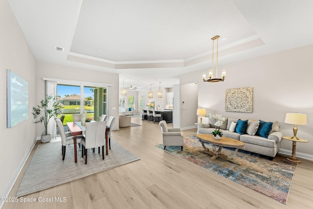 living area with an inviting chandelier, a raised ceiling, baseboards, light wood-type flooring, and visible vents