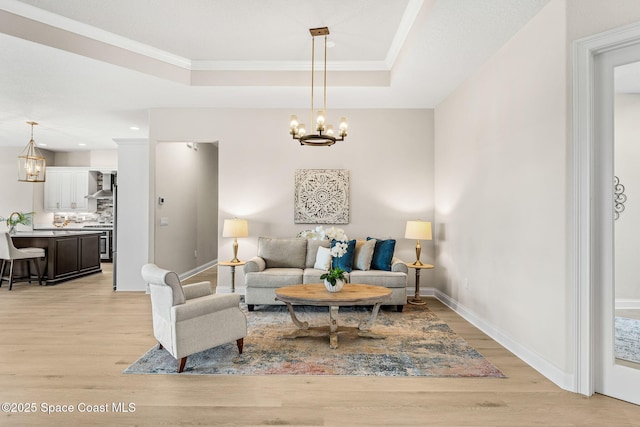 living room with light wood-type flooring, ornamental molding, baseboards, and a notable chandelier
