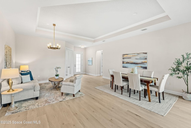 living area with crown molding, a notable chandelier, a raised ceiling, baseboards, and wood finished floors