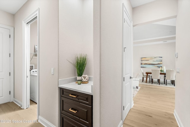 hallway featuring washer / clothes dryer, baseboards, and light wood-style floors