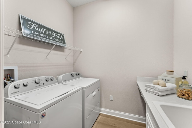 laundry room with laundry area, washing machine and clothes dryer, a sink, baseboards, and light wood-style flooring