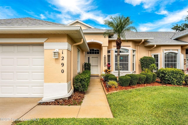 entrance to property with an attached garage, a yard, a shingled roof, and stucco siding
