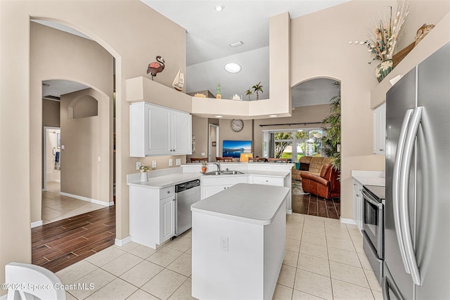 kitchen featuring a sink, high vaulted ceiling, light countertops, arched walkways, and appliances with stainless steel finishes