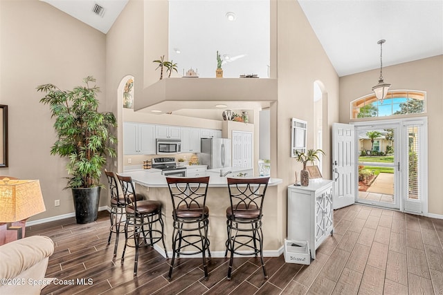 kitchen featuring wood tiled floor, visible vents, stainless steel appliances, and high vaulted ceiling