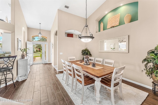 dining room featuring a towering ceiling, arched walkways, dark wood-style flooring, and baseboards