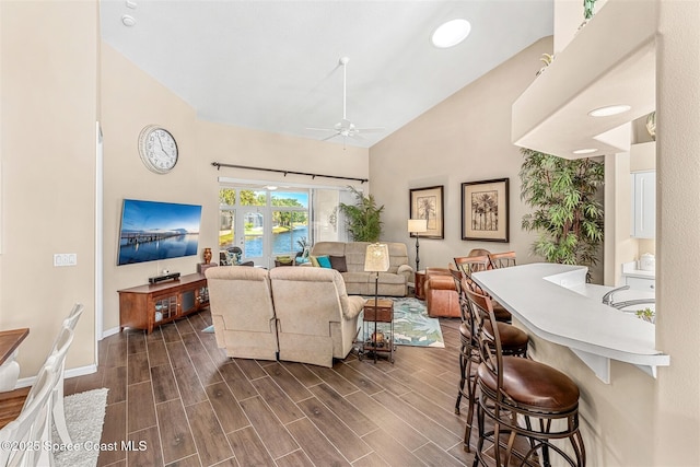 living room with ceiling fan, high vaulted ceiling, dark wood-style floors, and baseboards