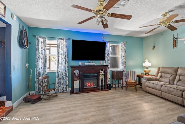 living room featuring a glass covered fireplace, a ceiling fan, wood finished floors, and a textured ceiling