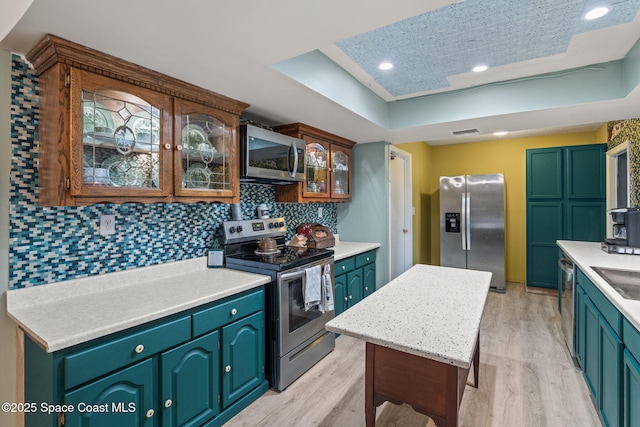 kitchen with tasteful backsplash, light wood-style flooring, a tray ceiling, light countertops, and appliances with stainless steel finishes