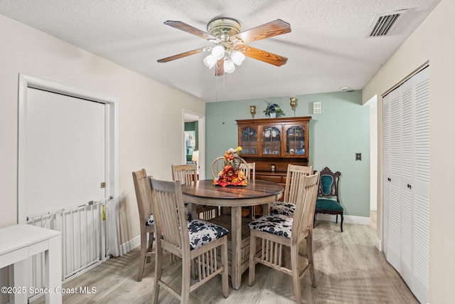 dining room featuring light wood finished floors, a textured ceiling, baseboards, visible vents, and ceiling fan