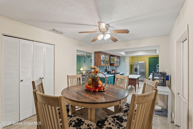 dining room featuring a textured ceiling, light wood-type flooring, visible vents, and a ceiling fan