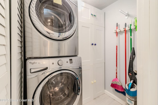 laundry area with baseboards, stacked washing maching and dryer, and cabinet space