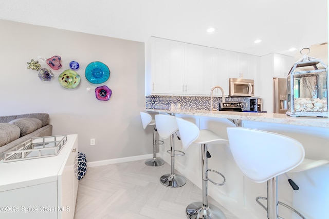 kitchen featuring recessed lighting, white cabinets, a kitchen breakfast bar, backsplash, and appliances with stainless steel finishes