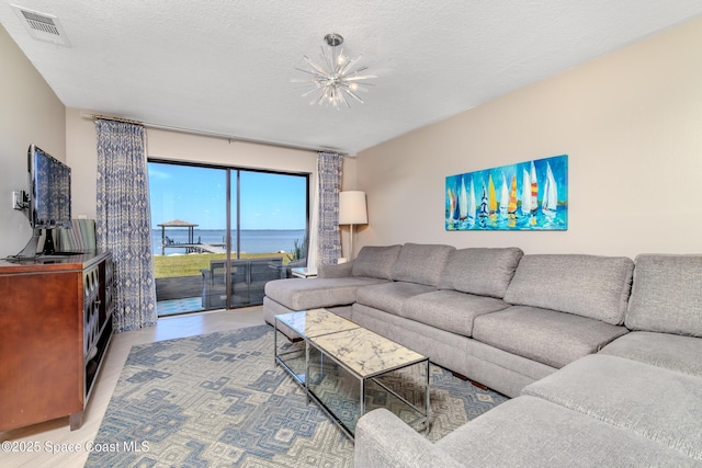 living room with wood finished floors, visible vents, a water view, a textured ceiling, and a notable chandelier