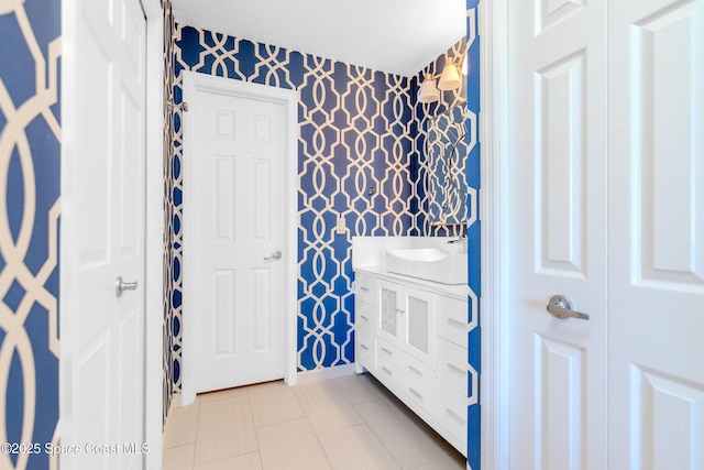 bathroom with wallpapered walls, baseboards, tile patterned floors, and vanity
