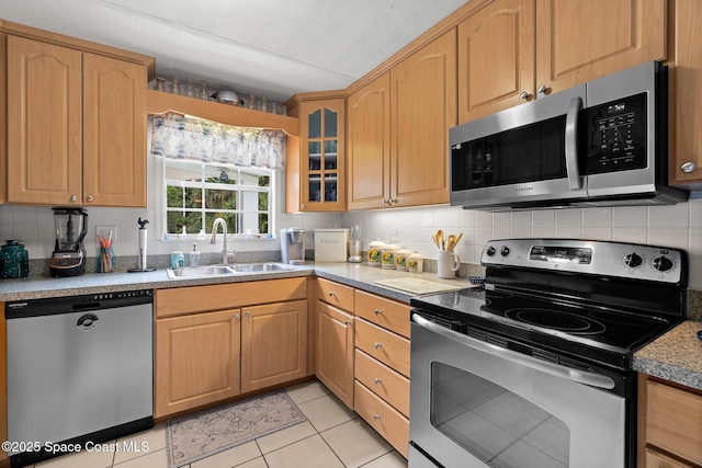 kitchen featuring light tile patterned flooring, glass insert cabinets, a sink, appliances with stainless steel finishes, and backsplash