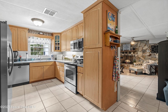 kitchen with visible vents, glass insert cabinets, a stone fireplace, a sink, and stainless steel appliances