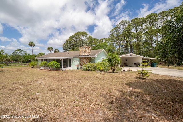 ranch-style home with driveway, a chimney, a front yard, a sunroom, and a carport