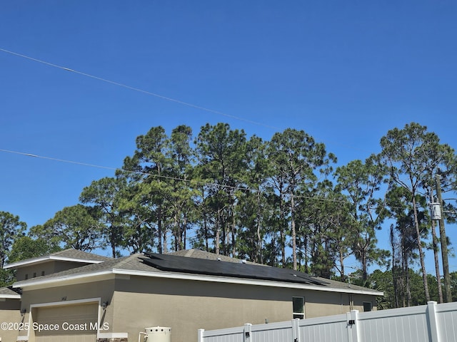 view of home's exterior featuring roof mounted solar panels, fence private yard, an attached garage, and stucco siding