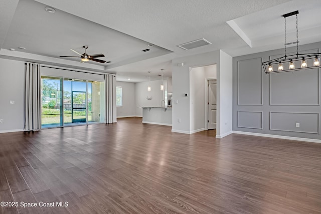unfurnished living room featuring baseboards, a ceiling fan, dark wood-type flooring, and a textured ceiling
