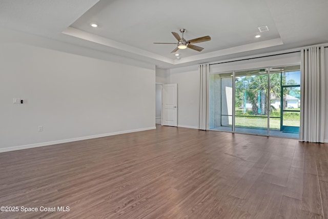 empty room featuring recessed lighting, a tray ceiling, wood finished floors, visible vents, and a ceiling fan