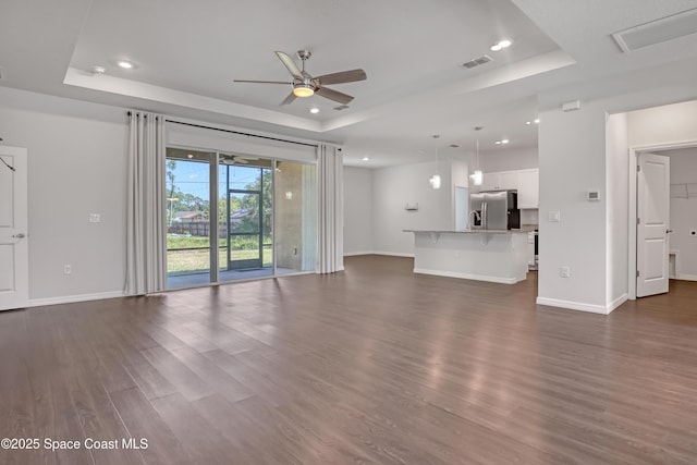 unfurnished living room with baseboards, a tray ceiling, dark wood-type flooring, and ceiling fan