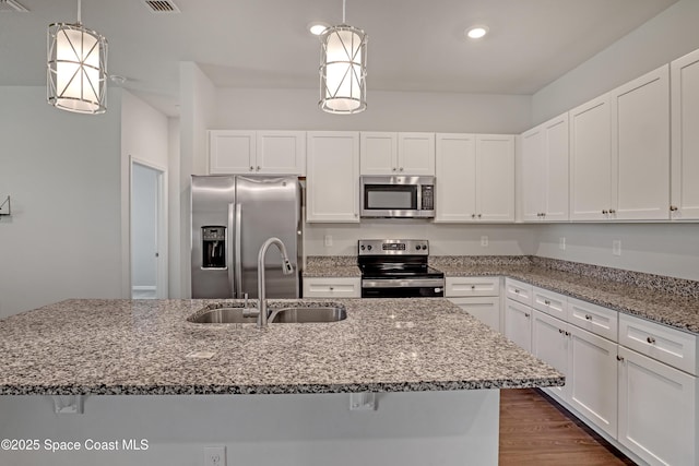 kitchen featuring white cabinets, appliances with stainless steel finishes, light stone counters, and a sink
