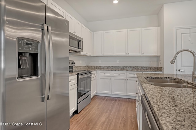 kitchen with white cabinets, stainless steel appliances, light wood-style flooring, a sink, and light stone counters